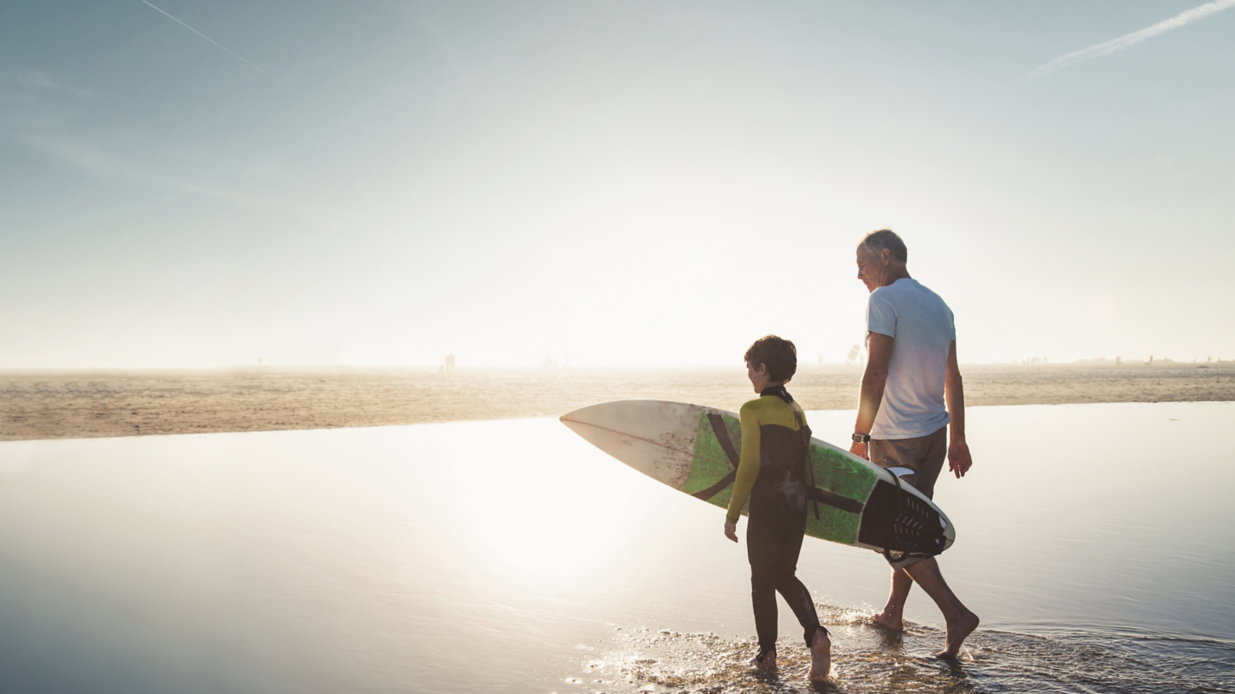 Man walking with grandson carrying surf board