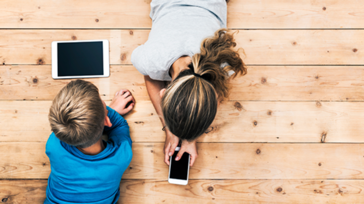 Top view image of two kids lying on the floor and playing with tablet and smartphone watching movie or gaming. Mockup or template for web or application design.