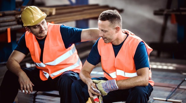 Sad manual worker being consoled by his colleague in aluminum mill.