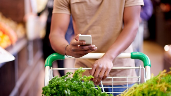 A person using a mobile phone while pushing their grocery trolley