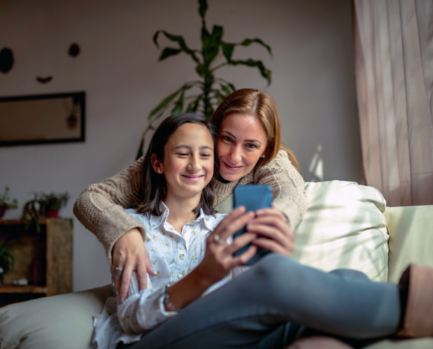 Mother and daughter sitting on a couch at home using a smartphone